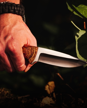 Ręka trzymająca nóż myśliwski, na tle zielonych liści. Ręka trzymająca nóż myśliwski, na tle zielonych liści.